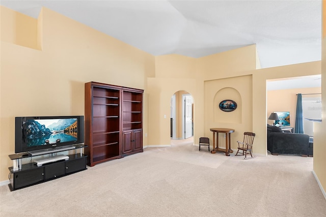 carpeted living area with arched walkways, baseboards, and a towering ceiling
