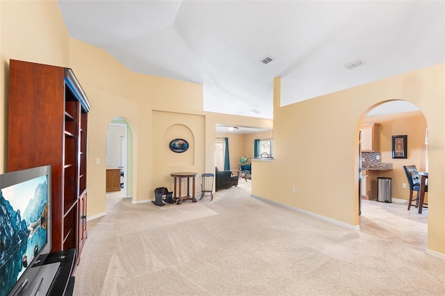 living room featuring arched walkways, visible vents, lofted ceiling, and light colored carpet