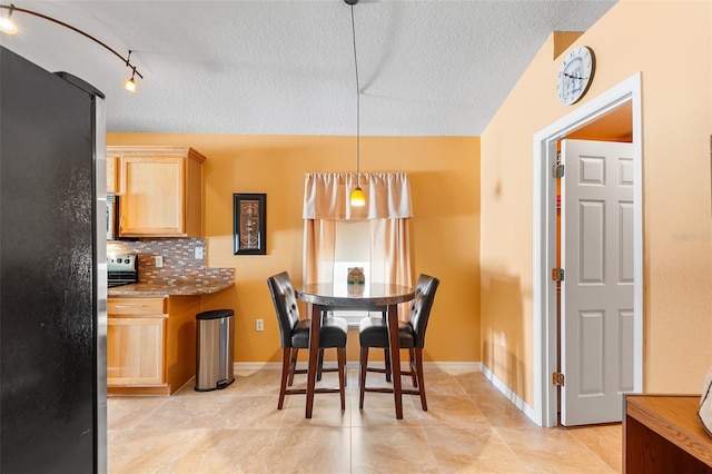 dining space featuring light tile patterned flooring, a textured ceiling, track lighting, and baseboards