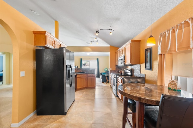 kitchen featuring dark countertops, arched walkways, stainless steel appliances, lofted ceiling, and tasteful backsplash