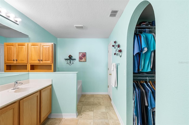 full bathroom with a bath, visible vents, a textured ceiling, vanity, and a spacious closet