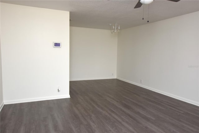 empty room featuring baseboards, ceiling fan with notable chandelier, and dark wood finished floors