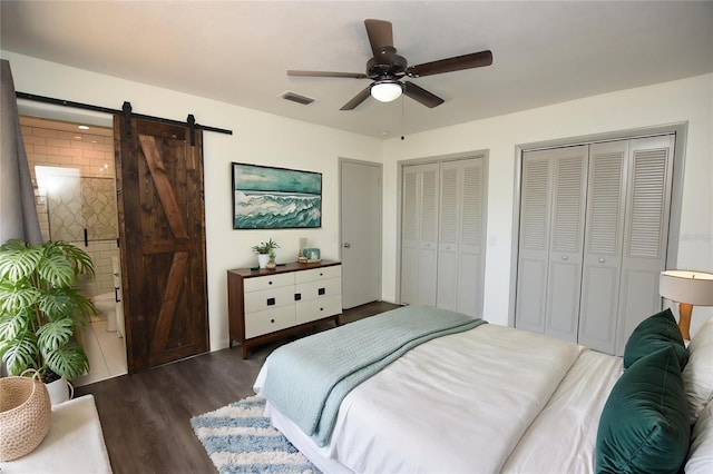 bedroom featuring a ceiling fan, visible vents, wood finished floors, a barn door, and multiple closets