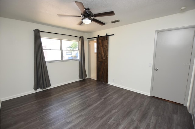 unfurnished bedroom with visible vents, baseboards, dark wood-type flooring, a barn door, and a ceiling fan