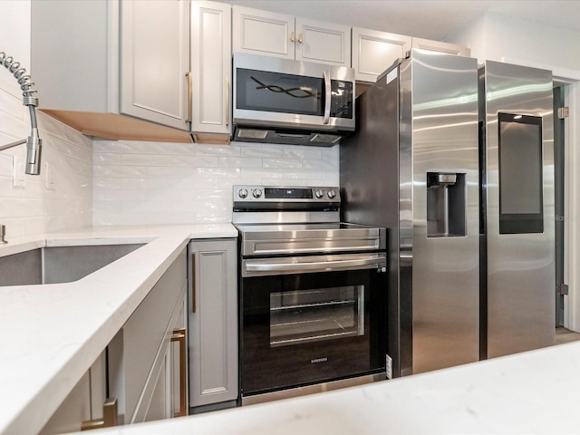 502 Duchess Dr, Lakeland, FL 33803 - kitchen featuring backsplash, gray cabinetry, light stone counters, a sink, and stainless steel appliances