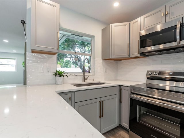 502 Duchess Dr, Lakeland, FL 33803 - kitchen featuring decorative backsplash, light stone counters, a sink, gray cabinetry, and stainless steel appliances