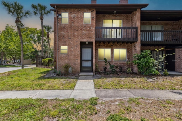 townhome / multi-family property with a chimney, brick siding, a balcony, and a front yard