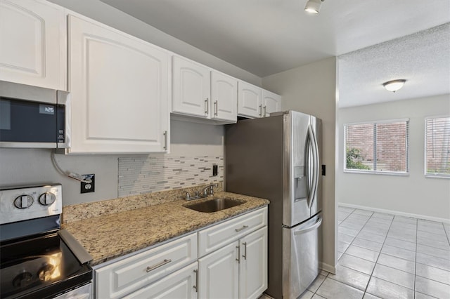kitchen featuring appliances with stainless steel finishes, light tile patterned flooring, a sink, white cabinetry, and tasteful backsplash