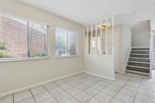spare room with light tile patterned floors, a textured ceiling, baseboards, and stairs
