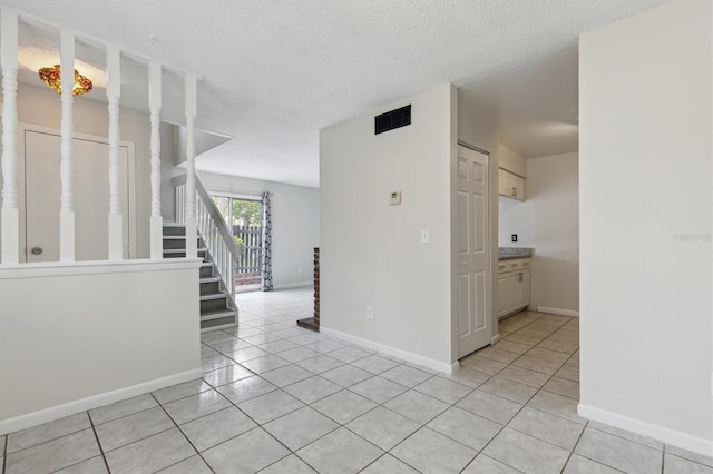 unfurnished room featuring light tile patterned flooring, stairs, baseboards, and a textured ceiling