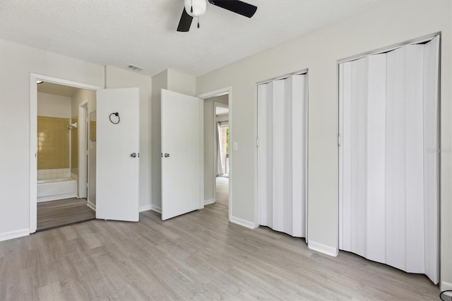 unfurnished bedroom with light wood-type flooring, two closets, baseboards, and ensuite bathroom