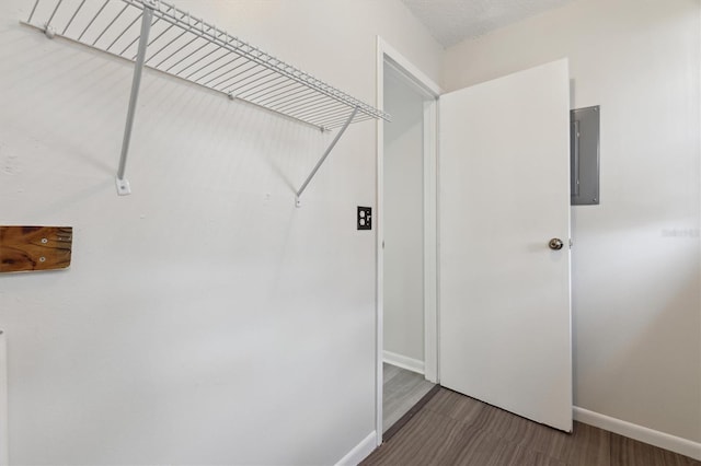 laundry area with electric panel, baseboards, and wood finished floors