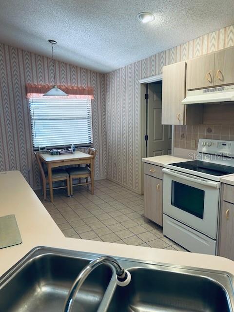 kitchen with white electric range, a textured ceiling, under cabinet range hood, and wallpapered walls