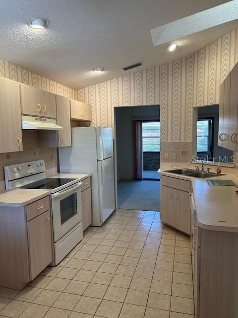 kitchen with wallpapered walls, light countertops, under cabinet range hood, electric stove, and a skylight