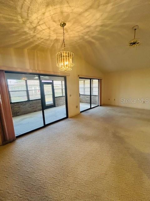 empty room with a notable chandelier, light carpet, and lofted ceiling