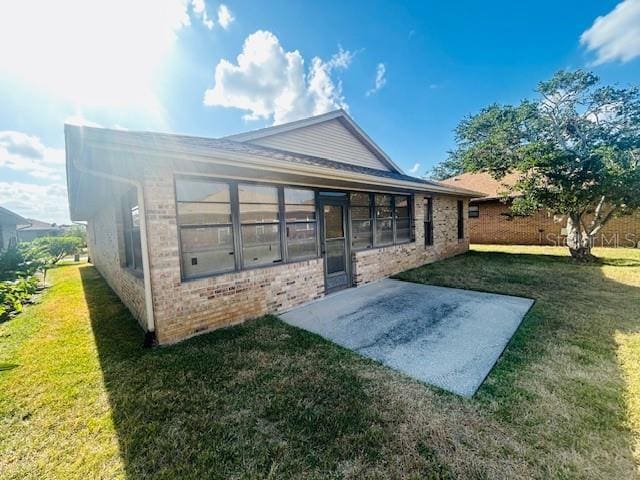 back of property featuring a lawn, a patio area, and brick siding