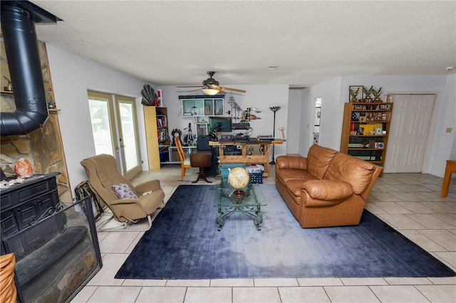 living area with a textured ceiling, tile patterned flooring, a wood stove, and ceiling fan