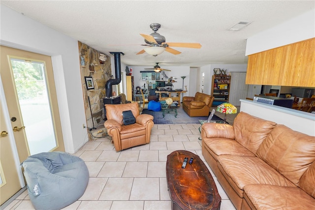 living area featuring a wood stove, a textured ceiling, a ceiling fan, light tile patterned floors, and visible vents