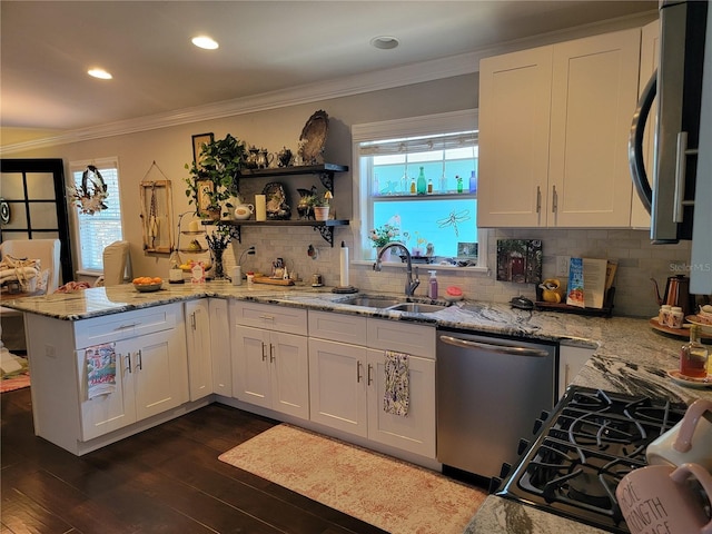 kitchen featuring white cabinets, appliances with stainless steel finishes, a sink, a peninsula, and ornamental molding