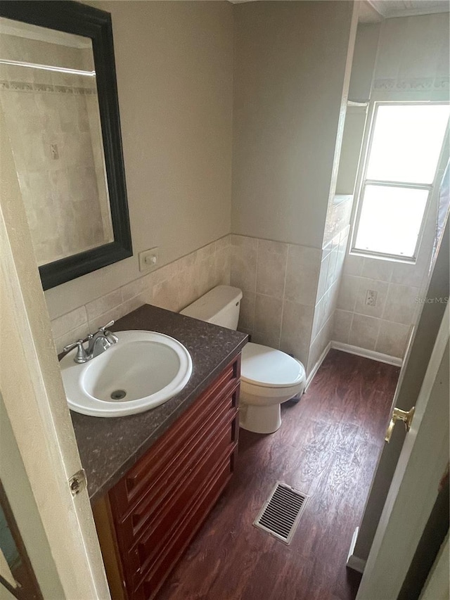 bathroom with vanity, toilet, tile walls, wood finished floors, and visible vents