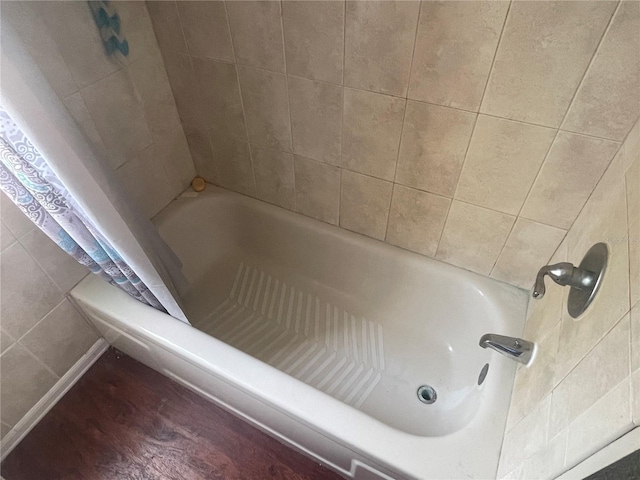 full bath featuring a shower with curtain, wood finished floors, and a tub to relax in