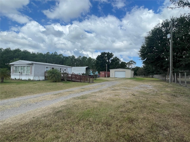 view of yard with driveway, an outbuilding, a wooden deck, a detached garage, and fence