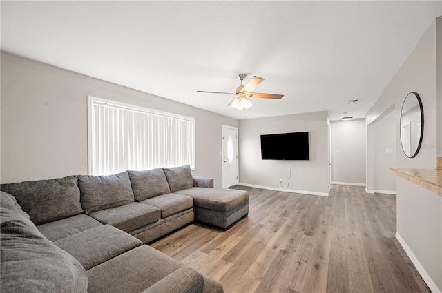 living area with light wood finished floors, a ceiling fan, and baseboards