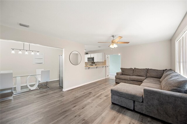 living room with light wood finished floors, a ceiling fan, and baseboards