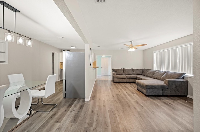 living area featuring baseboards, light wood-style floors, and a ceiling fan
