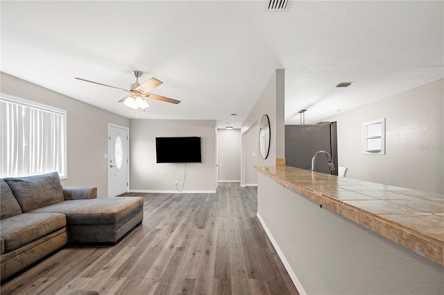 living area with a ceiling fan, light wood-style floors, baseboards, and healthy amount of natural light