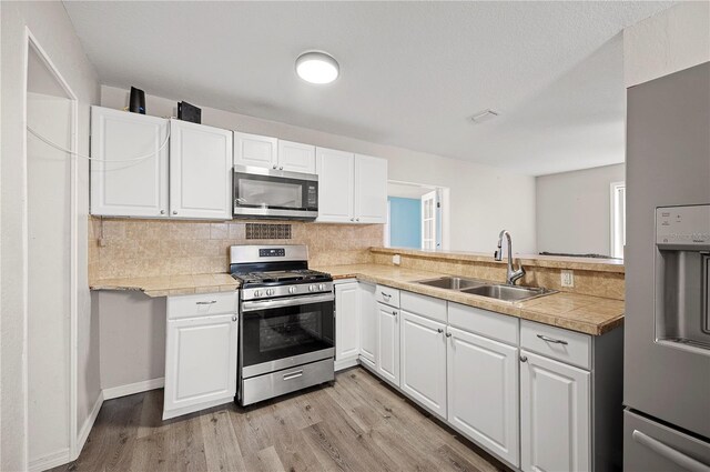 kitchen with stainless steel appliances, a sink, light wood finished floors, and white cabinets
