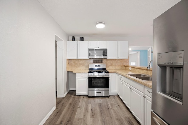 kitchen with stainless steel appliances, a sink, light wood finished floors, decorative backsplash, and white cabinets