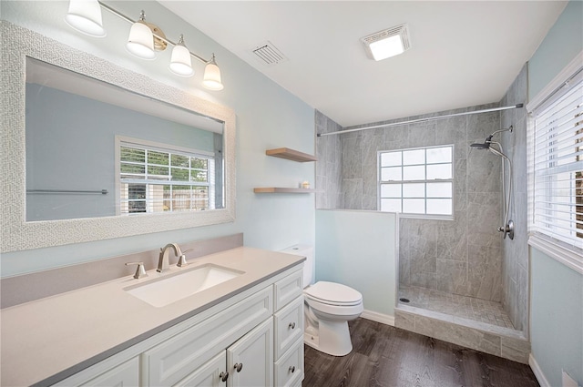 full bathroom featuring toilet, wood finished floors, a tile shower, and vanity
