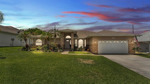 ranch-style home featuring stucco siding, brick siding, concrete driveway, an attached garage, and a yard