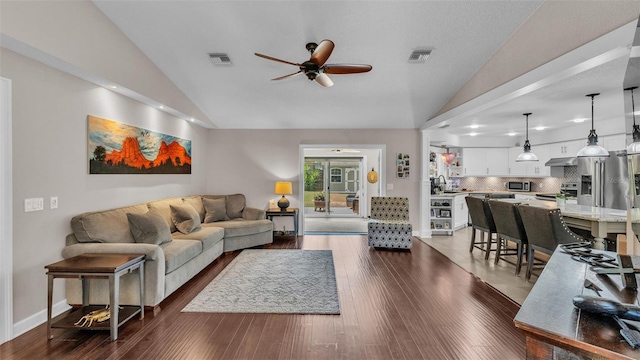 living area with a ceiling fan, visible vents, vaulted ceiling, baseboards, and dark wood-style floors