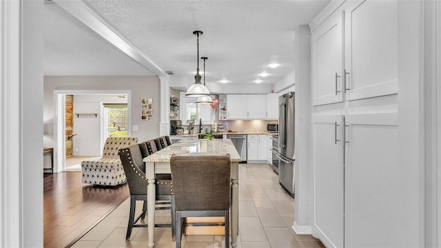 kitchen with decorative backsplash, light stone countertops, white cabinetry, hanging light fixtures, and stainless steel appliances