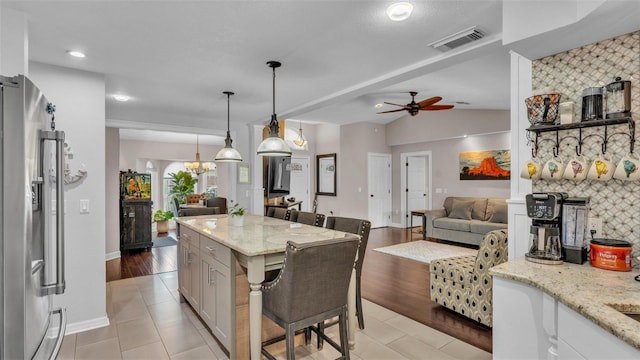 kitchen featuring stainless steel fridge with ice dispenser, light stone countertops, open floor plan, and visible vents