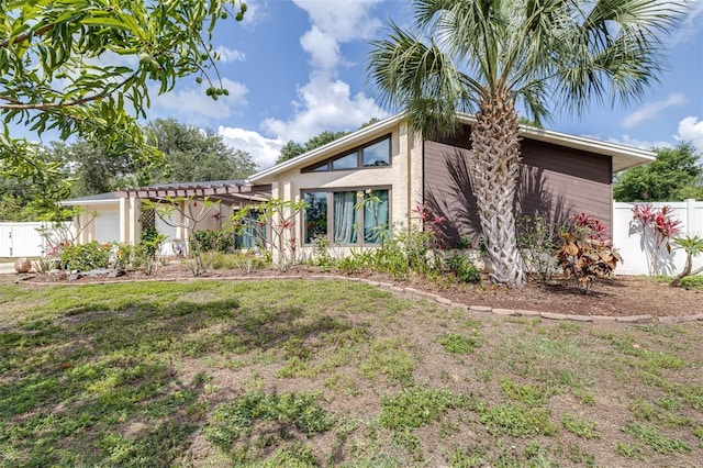mid-century home featuring a garage, fence, a pergola, a front yard, and stucco siding
