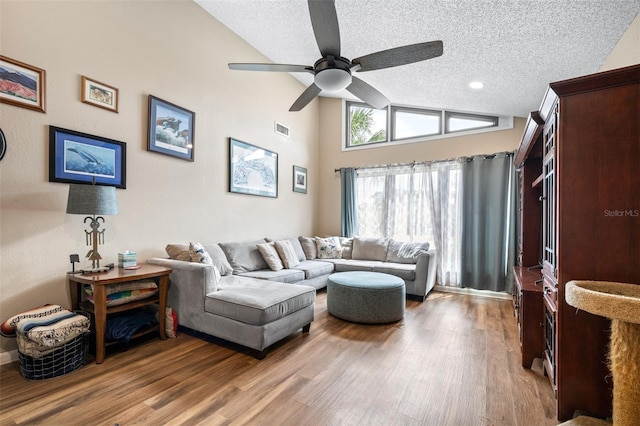 living area featuring a textured ceiling, a ceiling fan, wood finished floors, vaulted ceiling, and visible vents