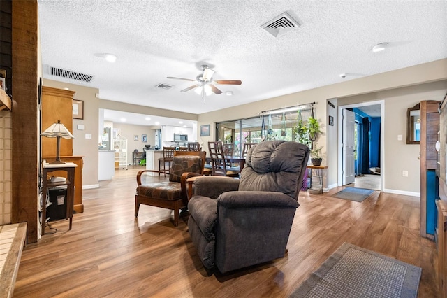 living area featuring visible vents, a ceiling fan, a textured ceiling, and wood finished floors
