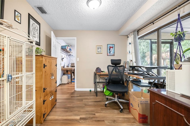 home office featuring light wood-style floors, a textured ceiling, baseboards, and visible vents
