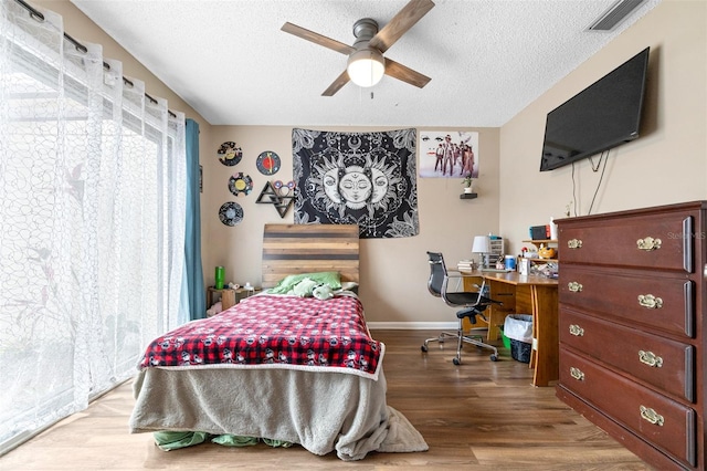 bedroom featuring baseboards, a textured ceiling, visible vents, and wood finished floors