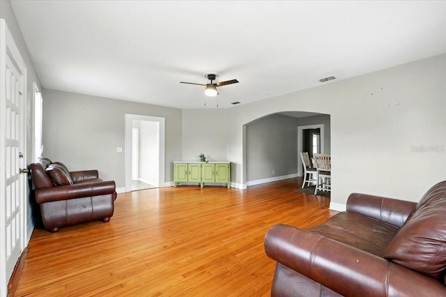 living area with visible vents, arched walkways, a ceiling fan, baseboards, and light wood-style floors