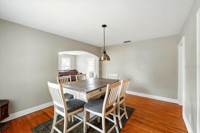 dining area featuring visible vents, wood finished floors, baseboards, and arched walkways