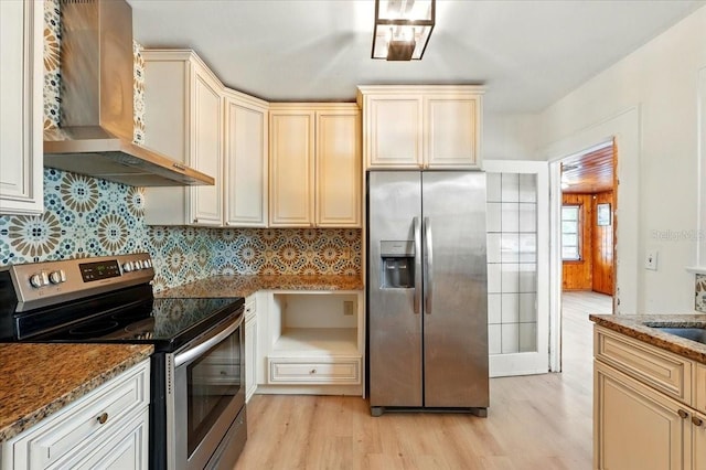 kitchen with light wood-type flooring, wall chimney range hood, tasteful backsplash, and appliances with stainless steel finishes