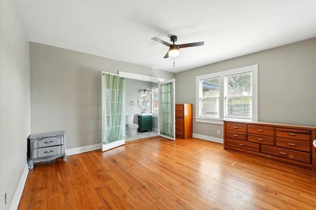 unfurnished bedroom featuring baseboards, light wood-style floors, ensuite bath, and a ceiling fan