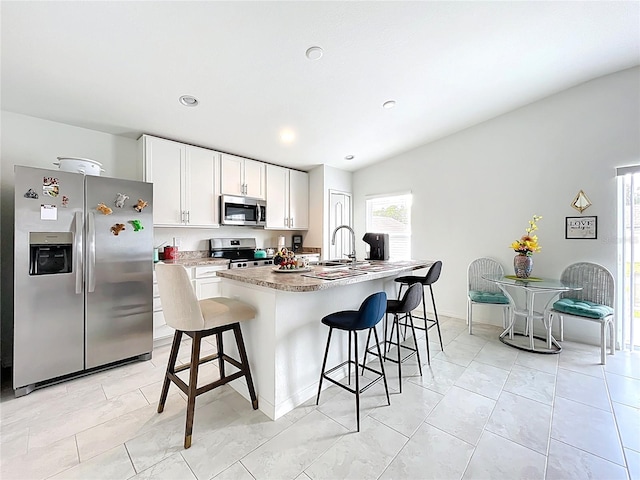 kitchen with a kitchen breakfast bar, a center island with sink, light countertops, white cabinets, and stainless steel appliances