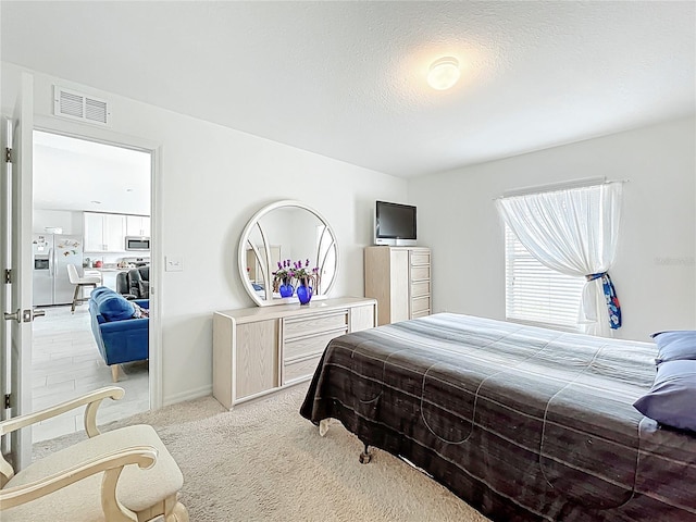 bedroom featuring visible vents, baseboards, light colored carpet, a textured ceiling, and stainless steel fridge with ice dispenser
