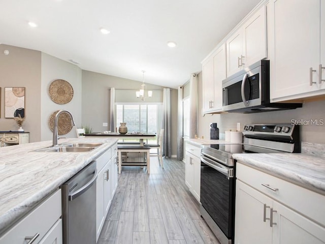 kitchen featuring appliances with stainless steel finishes, vaulted ceiling, a sink, light wood finished floors, and white cabinetry