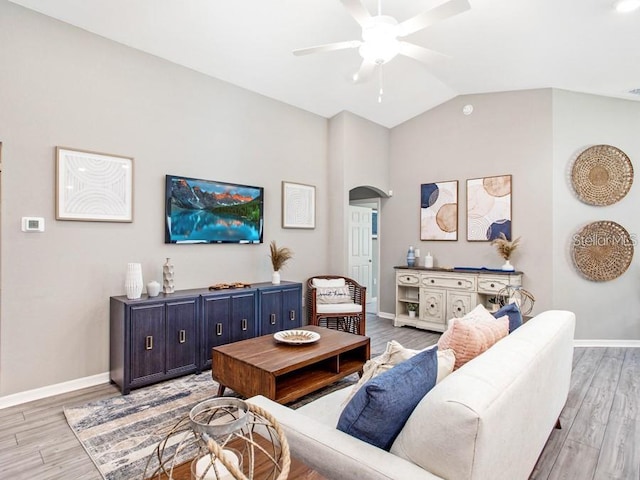 living area featuring ceiling fan, arched walkways, baseboards, lofted ceiling, and light wood-type flooring